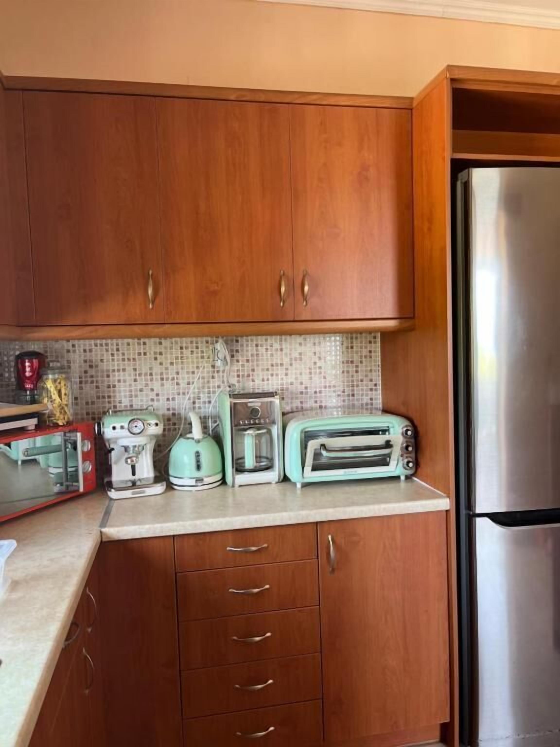 Una cocina con armarios de madera, un refrigerador de acero inoxidable, una cafetera, un tostador y una tetera.