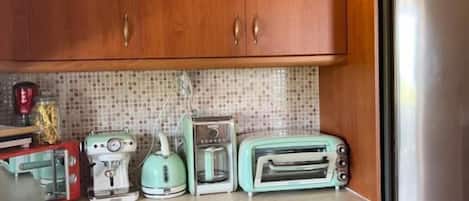 Una cocina con armarios de madera, un refrigerador de acero inoxidable, una cafetera, un tostador y una tetera.