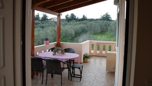 An open patio with a table and chairs, a view of greenery, and a wooden ceiling. - Angellinas Apartment (Chania)