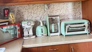 A kitchen with wooden cabinets, a tiled backsplash, and various appliances including a coffee maker, kettle, and toaster. - Angellinas Apartment (Chania)