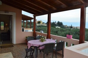 A covered outdoor area with a table and chairs, potted plants, and a view of the landscape. - Angellinas Apartment (Chania)