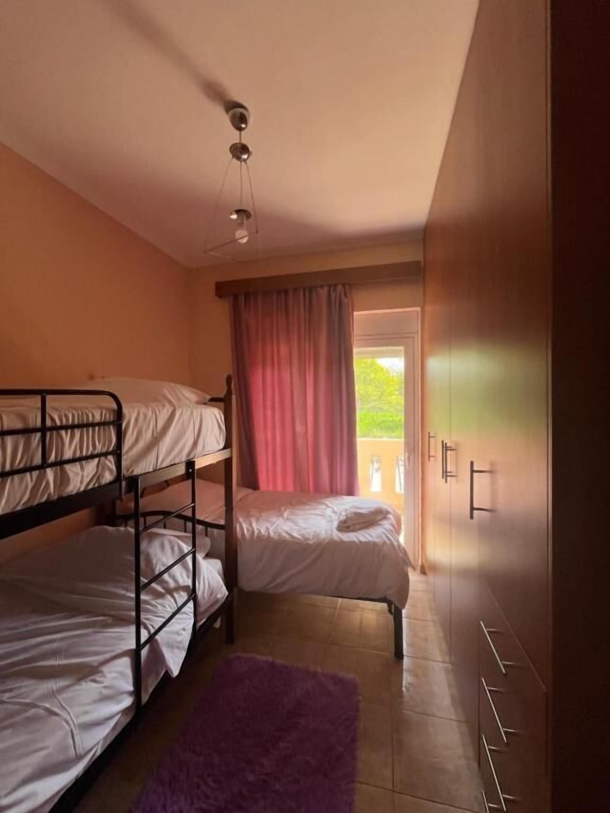 Ein Schlafsaalzimmer mit Etagenbetten, einem violetten Teppich und einem Fenster mit Vorhängen.