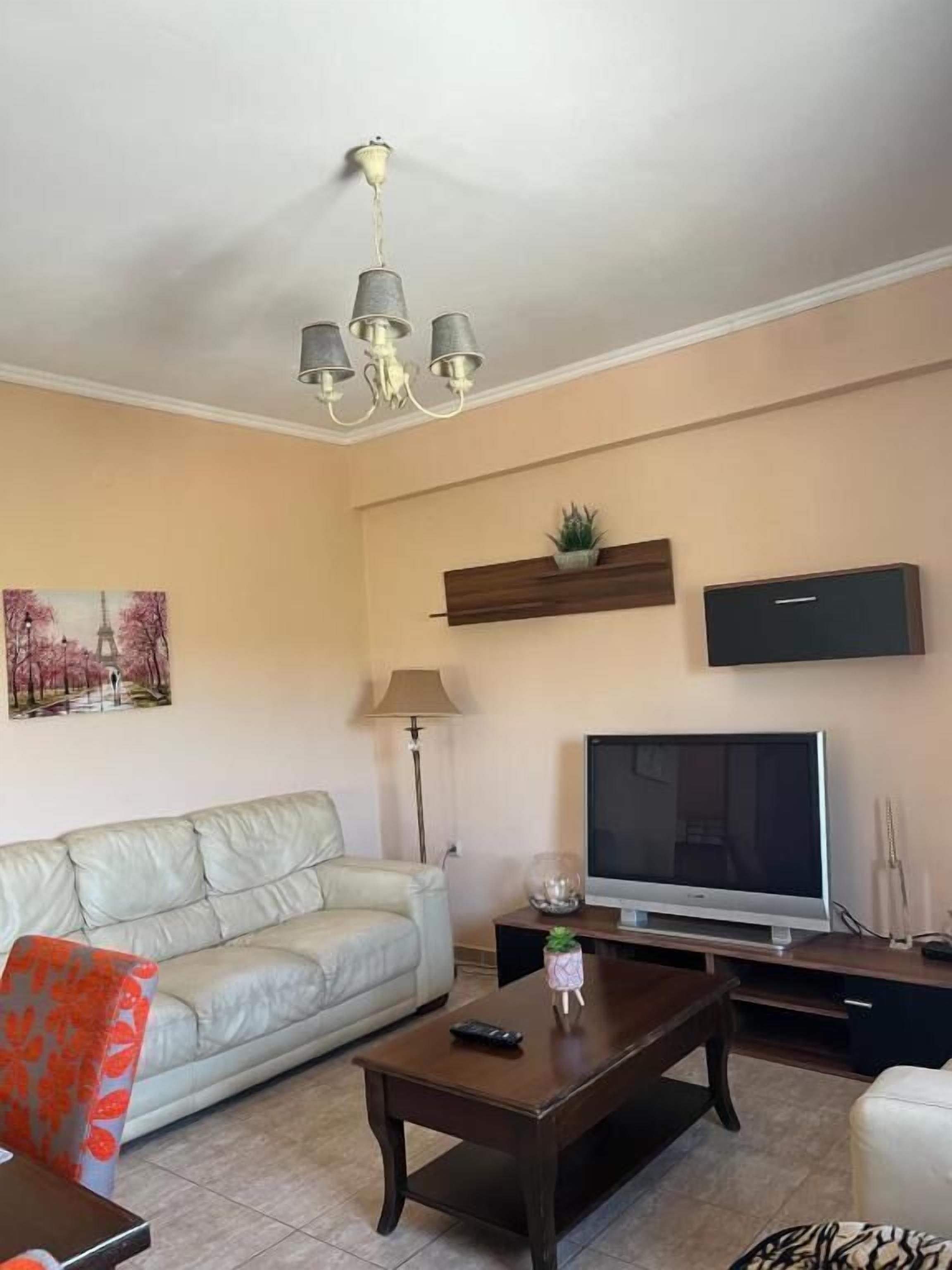 A living room with a sofa, a coffee table, a TV, a lamp, and a wall-mounted shelf with a plant.
