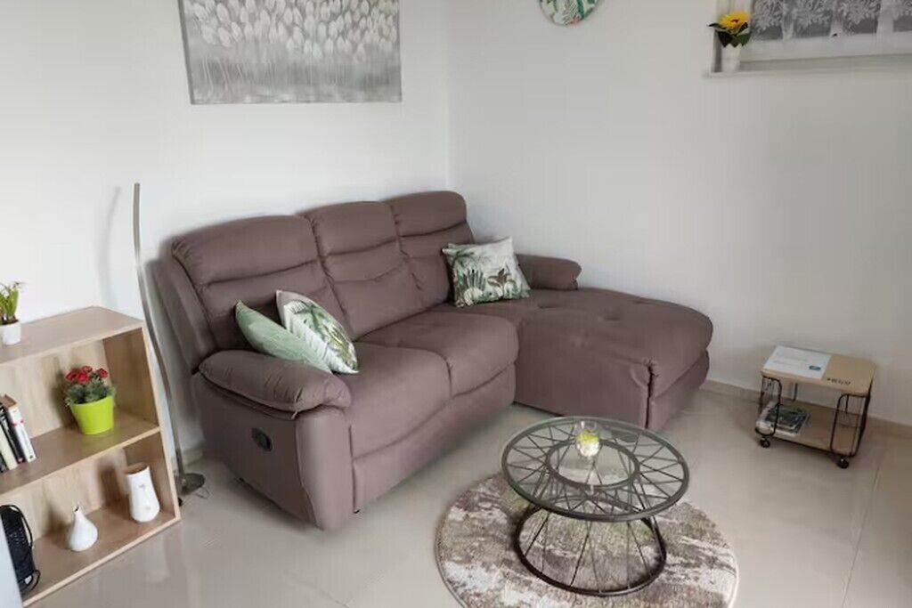 A modern living room with a brown sectional sofa, a glass coffee table, and a small bookshelf.