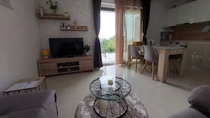 A living room with a TV, a glass coffee table, and a dining area with chairs. - Villa Madlen - Sea View Apartment 1 (Opatija)