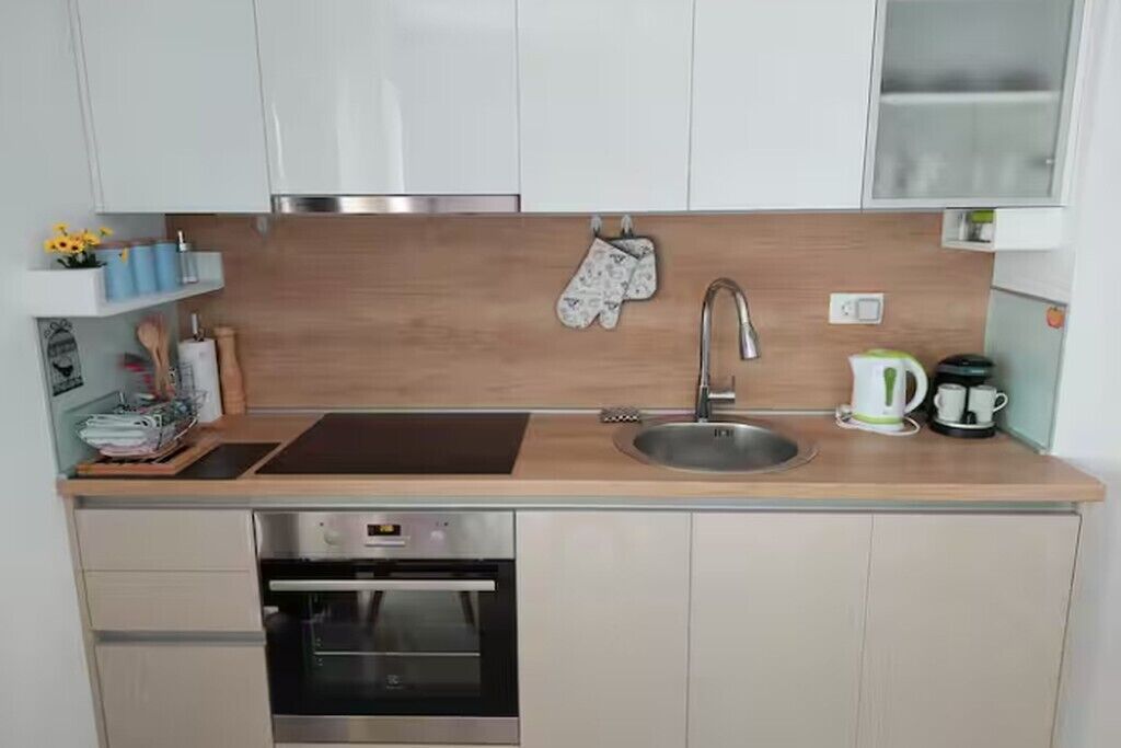 Ett kompakt kök med en inbyggd ugn, en diskho i rostfritt stål och en kaffebryggare.