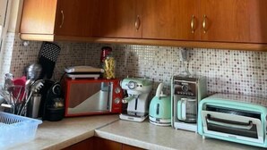 A kitchen with wooden cabinets, a unique textured ceiling light, and vintage appliances on the counter. - Angellinas Appartments (Chania)