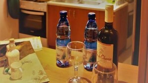 A kitchen with wooden cabinets, a window, and a table with bottles and glasses. - Angellinas Appartments (Chania)