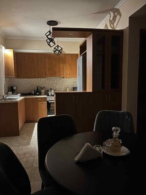 A modern kitchen with wooden cabinets, a central island, and a dining area with a table and chairs. - Angellinas Appartments (Chania)