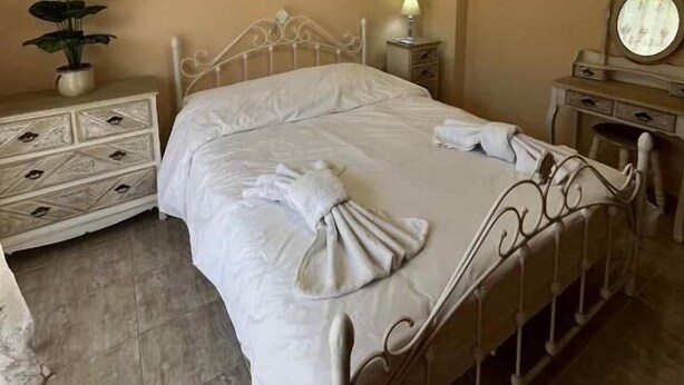 A neatly arranged bedroom with a bed, bedside tables, a dresser, a mirror, and a hanging light fixture. - Angellinas Appartments (Chania)