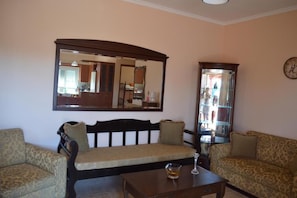 A living room with a sofa, a coffee table, a mirror, and a clock on the wall. - Angellinas Appartments (Chania)