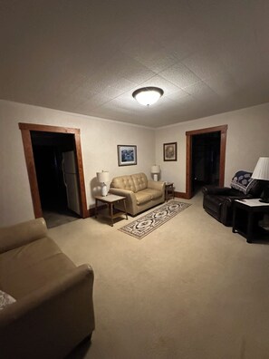 A living room with a beige sofa, a dark brown leather couch, and a patterned rug. There are two lamps and a framed picture on the wall. - Privacy & space to unwind in this brick 3 bed home just minutes to the Beach! (Supply)
