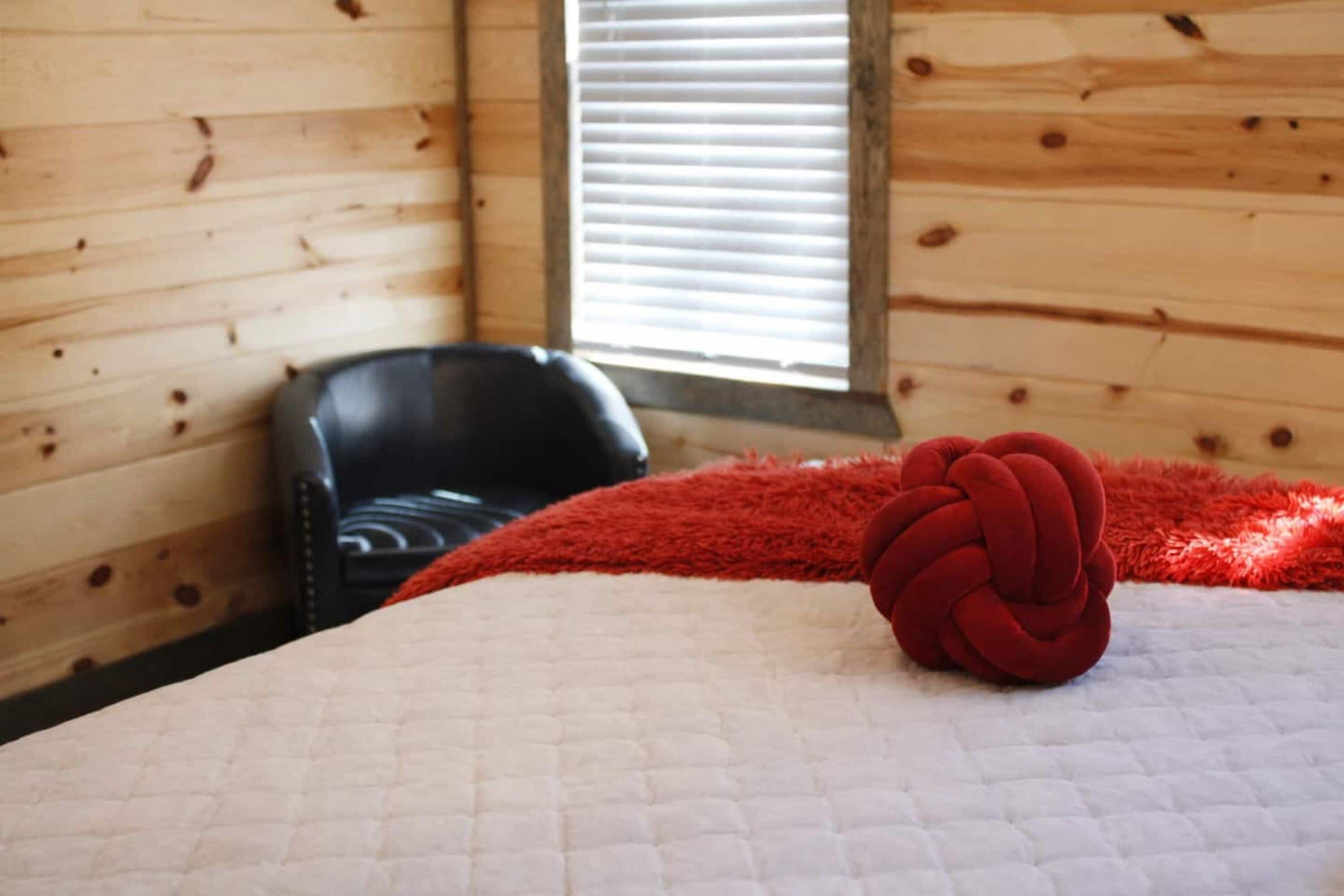 Une pièce dans une cabane en bois, avec un lit, une couverture rouge et une chaise noire.