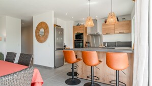 A modern kitchen with a central island, bar stools, and a dining area with wicker chairs. - Villa 'Lo Ginest' with Mountain View, Wi-Fi, and Air Conditioning (Villedieu)