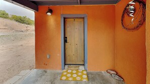 Una puerta de madera con un picaporte metálico, un felpudo estampado en amarillo y un aplique de pared.