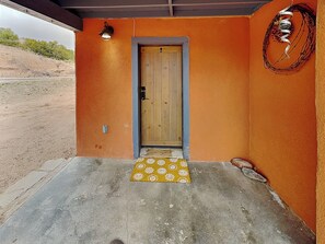Une porte en bois avec une poignée en métal, un paillasson jaune à motifs et un luminaire fixé au mur.