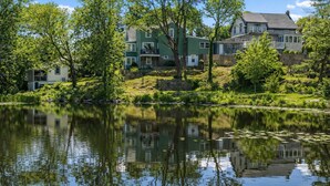 En fastighet vid sjön med flera hus, en stenmur och en spegelbild i vattnet.