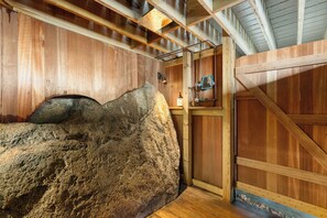 Een rustiek houten interieur met een grote rots, houten balken en een landelijke deur.