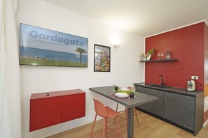 A compact kitchen with a red cabinet, a dining table with two chairs, and a red accent wall. - Pink Oleander Apartment (Sirmione)