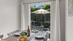 Ein Essbereich mit einem Tisch für vier Personen, einer Weinflasche und Blick auf den Garten durch eine geöffnete Tür.