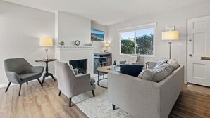Ein Wohnzimmer mit Kamin, Sofa, Sessel, Couchtisch und Fernseher.