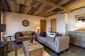 Ein gemütliches Wohnzimmer mit einer Couch, einem kleinen Tisch, einer Lampe und einer Uhr an der Wand.