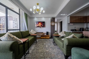Ein modernes Wohnzimmer mit grünen Sofas, einem an der Wand montierten Fernseher, einem Holztisch und einem gemusterten Teppich.