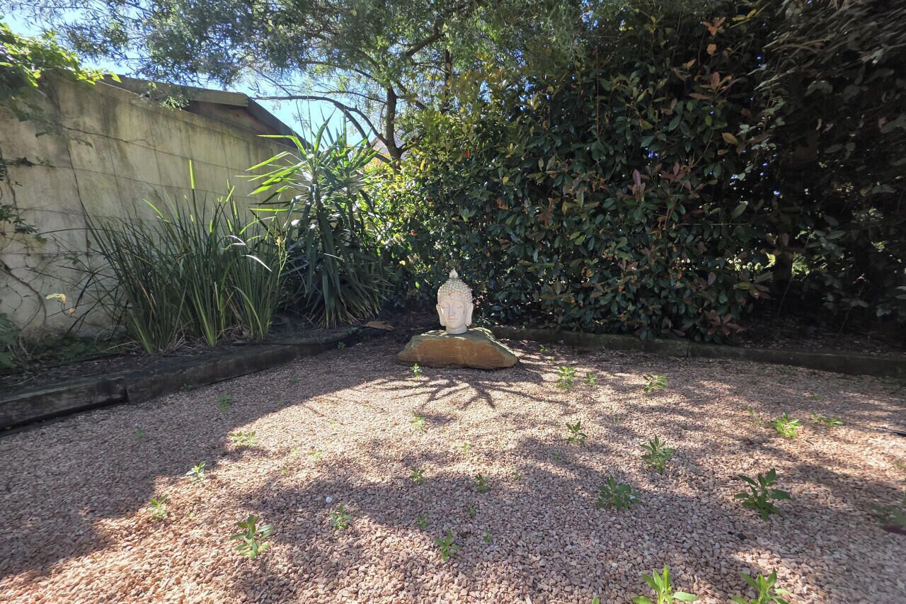 Un jardin agrémenté d’une structure en pierre, d’un sol recouvert de gravier et d’un feuillage dense.