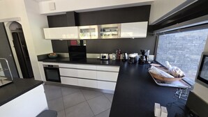 Una cucina moderna con mobili bianchi, un piano di lavoro nero e una finestra che si affaccia su un muro in mattoni.