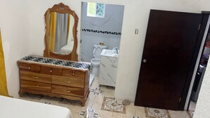 A bedroom with a wooden dresser, a bed, a bathroom with a toilet and sink, and a tiled floor. - Peaceful 1-bedroom apartment with AC in charming Ocho Rios (Ocho Rios)