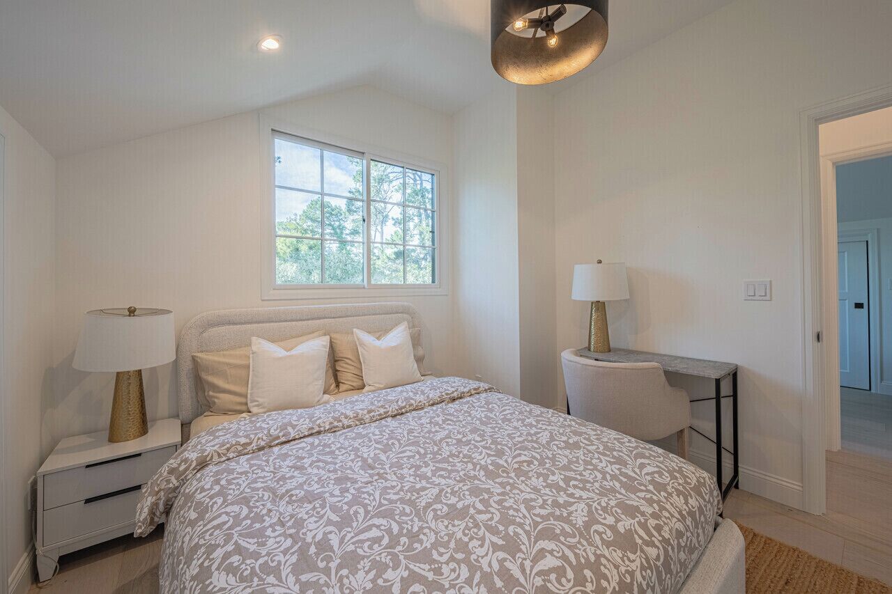 A bedroom with a bed, two bedside tables with lamps, a window, and a door leading to another room.