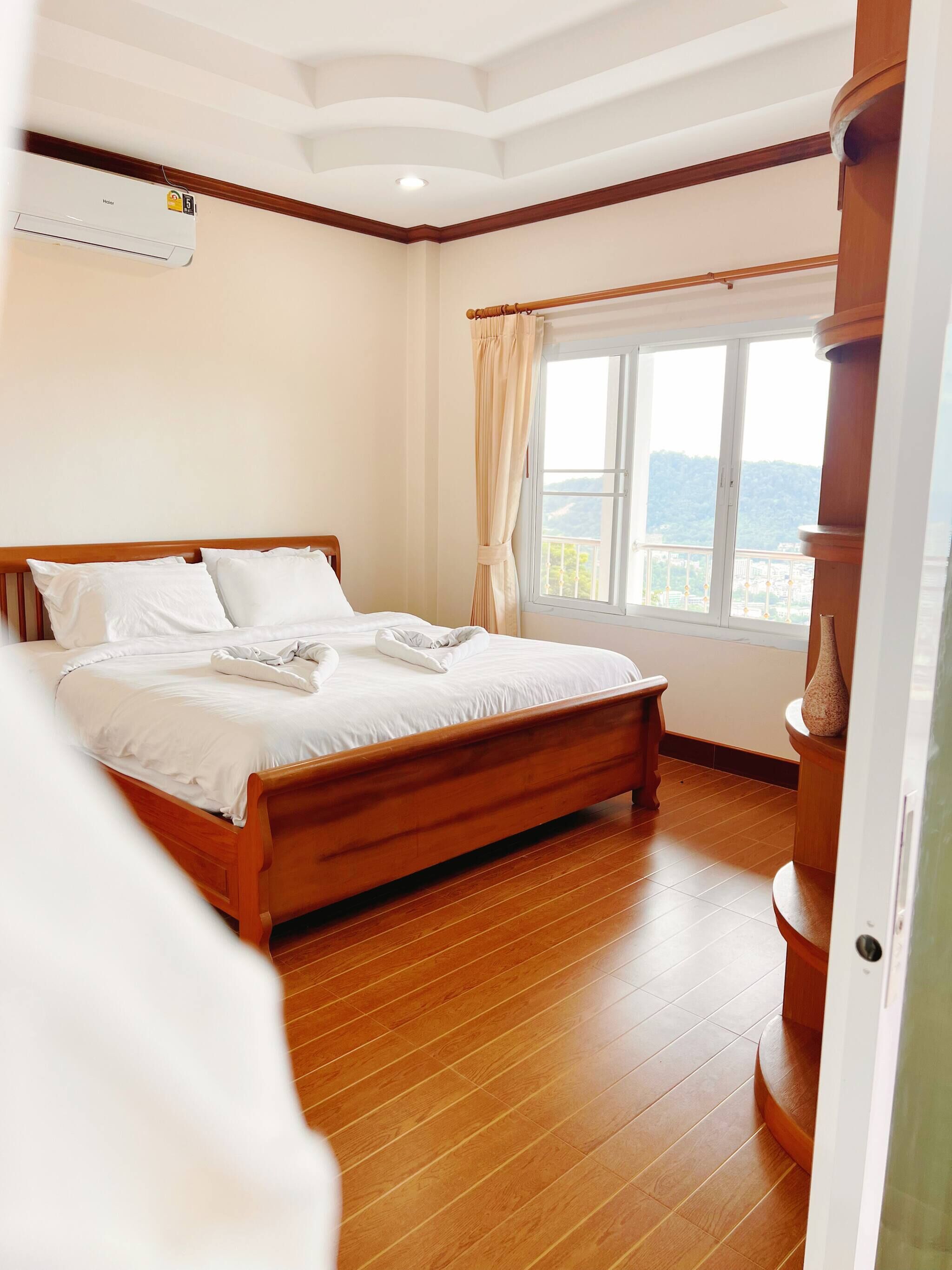 Ein Schlafzimmer mit einem Holzbett, einem Fenster mit Vorhängen und Blick ins Freie.