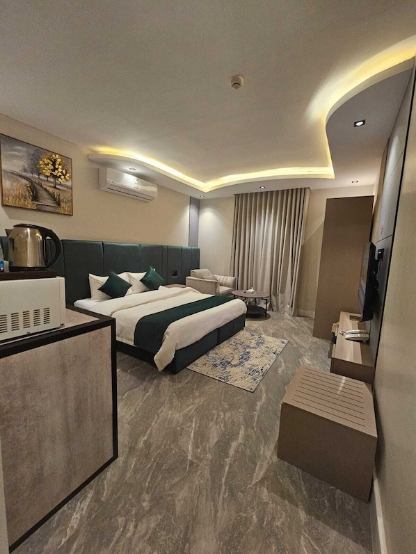 A modern hotel room with a large bed, a desk, a television, and an air conditioning unit.