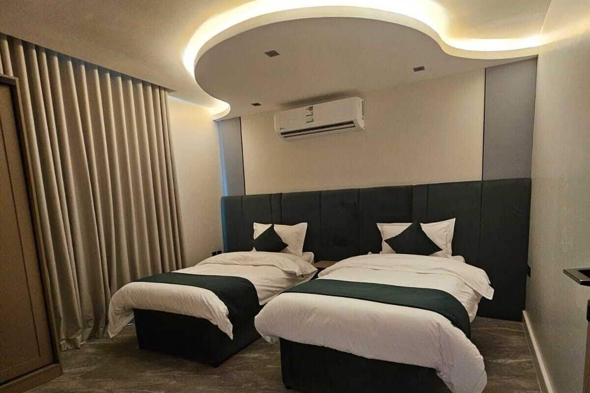 Habitación de hotel con dos camas, una lámpara de techo curva, un equipo de aire acondicionado y una cortina en la ventana.