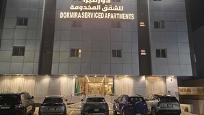 A building with a sign for dormitory serviced apartments. There are multiple cars parked in front. - dormira serviced apartments (Riyadh)