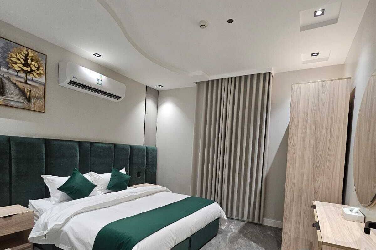 Una habitación de hotel moderna con una cama grande, una mesita de noche, un escritorio con una silla, un armario y un equipo de aire acondicionado.