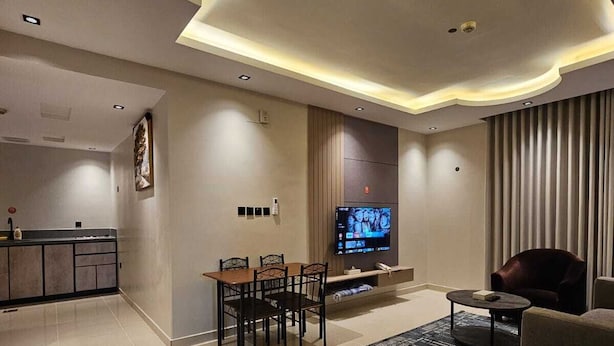 A modern living room with a flat-screen TV, a dining area, and a kitchen in the background. - dormira serviced apartments (Riyadh)