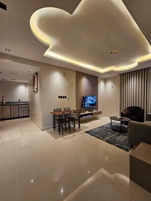 A modern living room with a flat-screen TV, a dining area, and a kitchen in the background. - dormira serviced apartments (Riyadh)