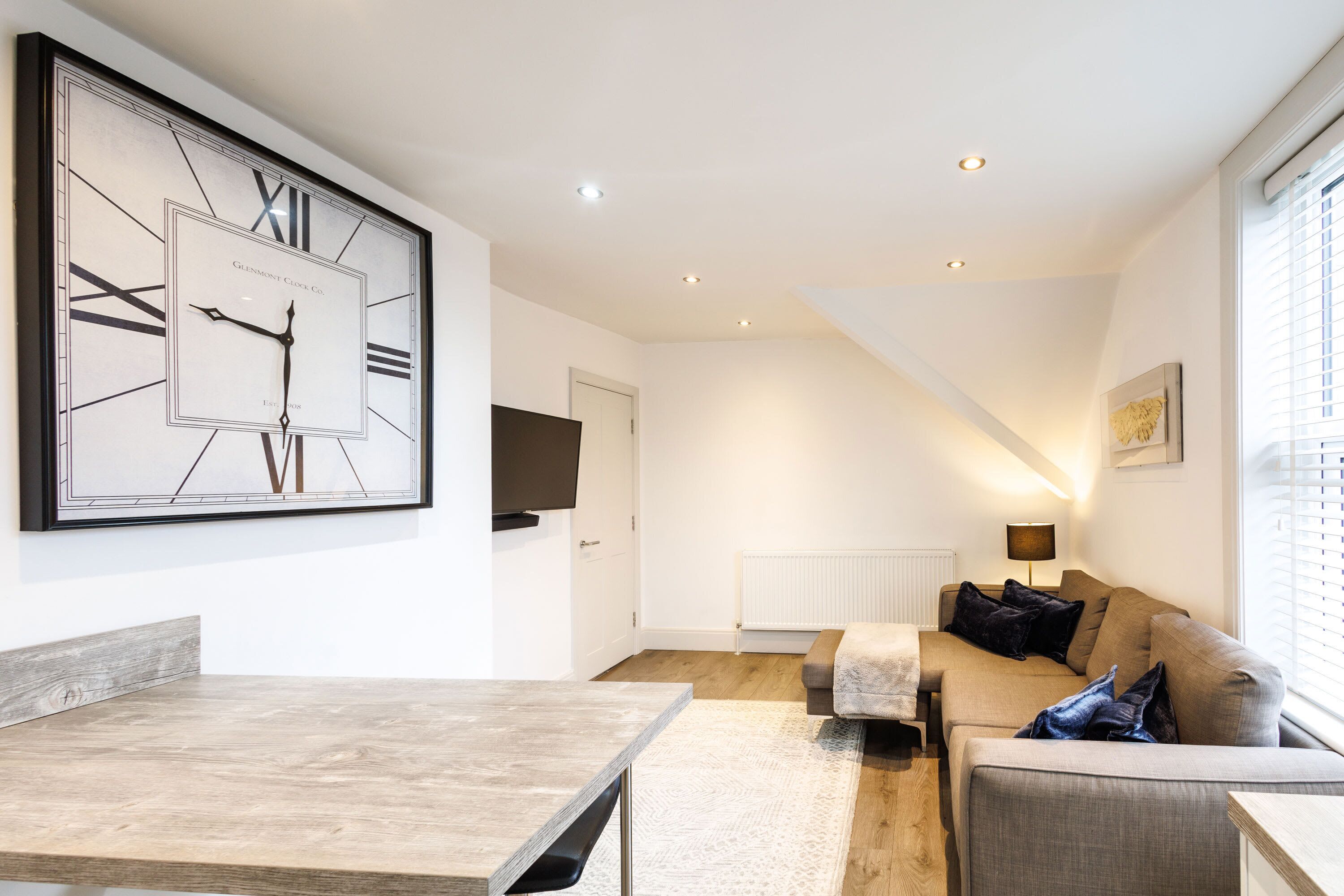 A modern living room with a large wall clock, a sofa, a coffee table, and a TV mounted on the wall.
