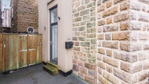 Un estrecho callejón con una puerta de madera, un muro de piedra y un acceso a un edificio.
