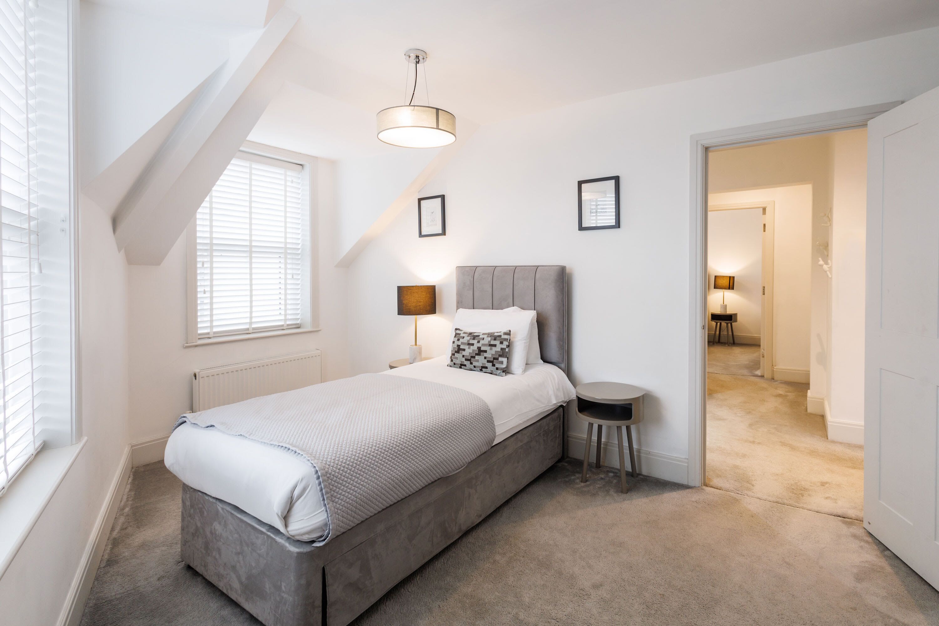 A bedroom with a bed, bedside table, lamp, and a view of another room.