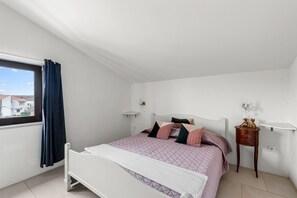 Un dormitorio con cama, mesita de noche, lámpara y ventana con cortinas.