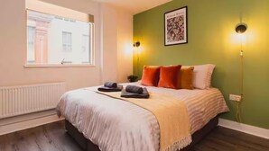 A bedroom with a bed, a window, a radiator, and a green wall with a picture. - Central 1-bed Apartment With Free Parking & Wifi (Leicester)