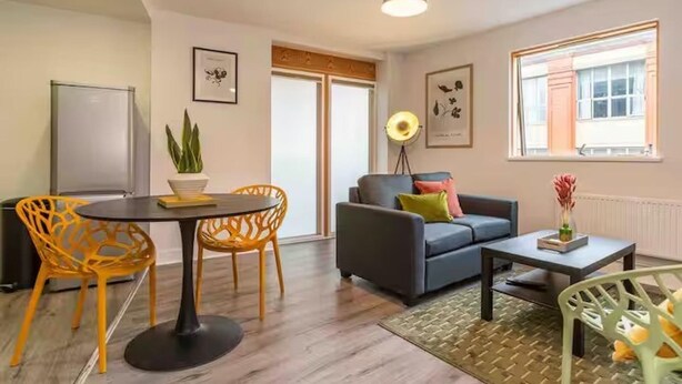 A modern living room with a sofa, two chairs, a coffee table, and a dining table. There are framed pictures on the walls and a floor lamp. - Central 1-bed Apartment With Free Parking & Wifi (Leicester)