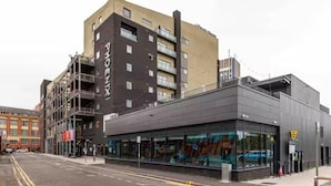 A modern building with a glass facade, a visible entrance, and a parking area in front. - Central 1-bed Apartment With Free Parking & Wifi (Leicester)