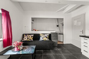 Ein kompakter Wohnbereich mit einer Couch, einem kleinen Tisch mit einer Vase und einer Küchenzeile.