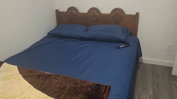 Un lit avec une couvre-lit bleue, une couverture marron et beige, et une tête de lit en bois.