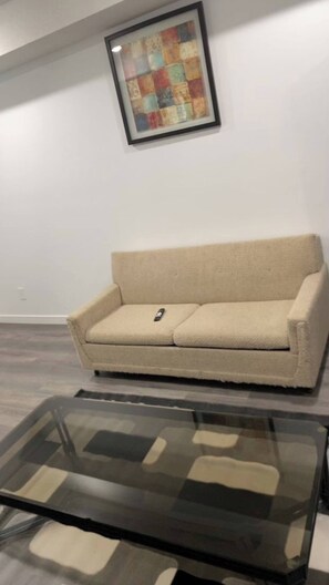 A living room with a beige sofa, a glass coffee table, and a colorful abstract painting on the wall. - Room-new Build 2025 Comfy Suite! (Edmonton)