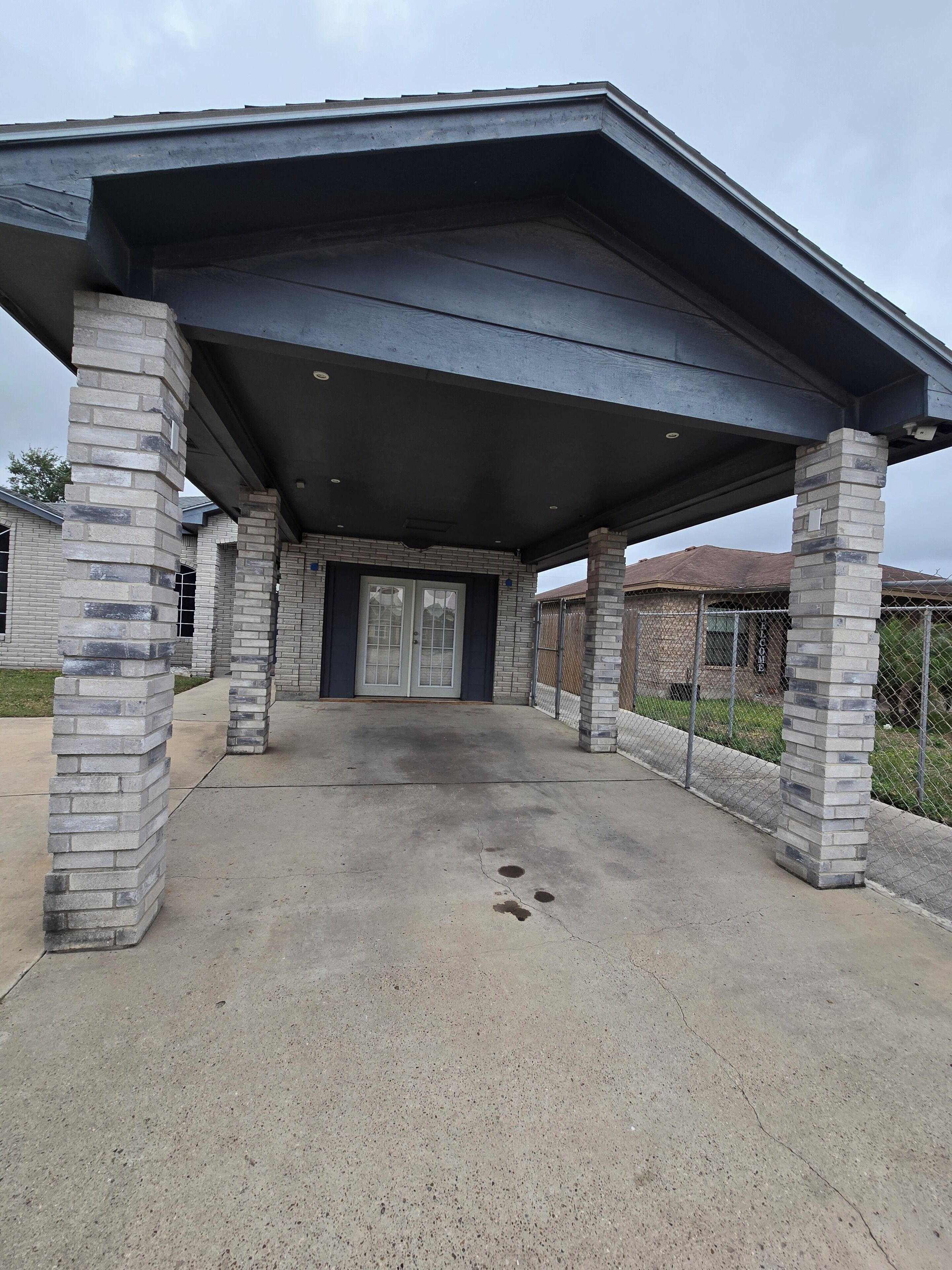 A covered outdoor area with a concrete floor, stone pillars, and a metal roof.