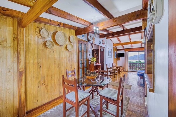 A wooden dining area with a glass table surrounded by chairs, a wooden ceiling with exposed beams, and a view of the outdoors through a door.